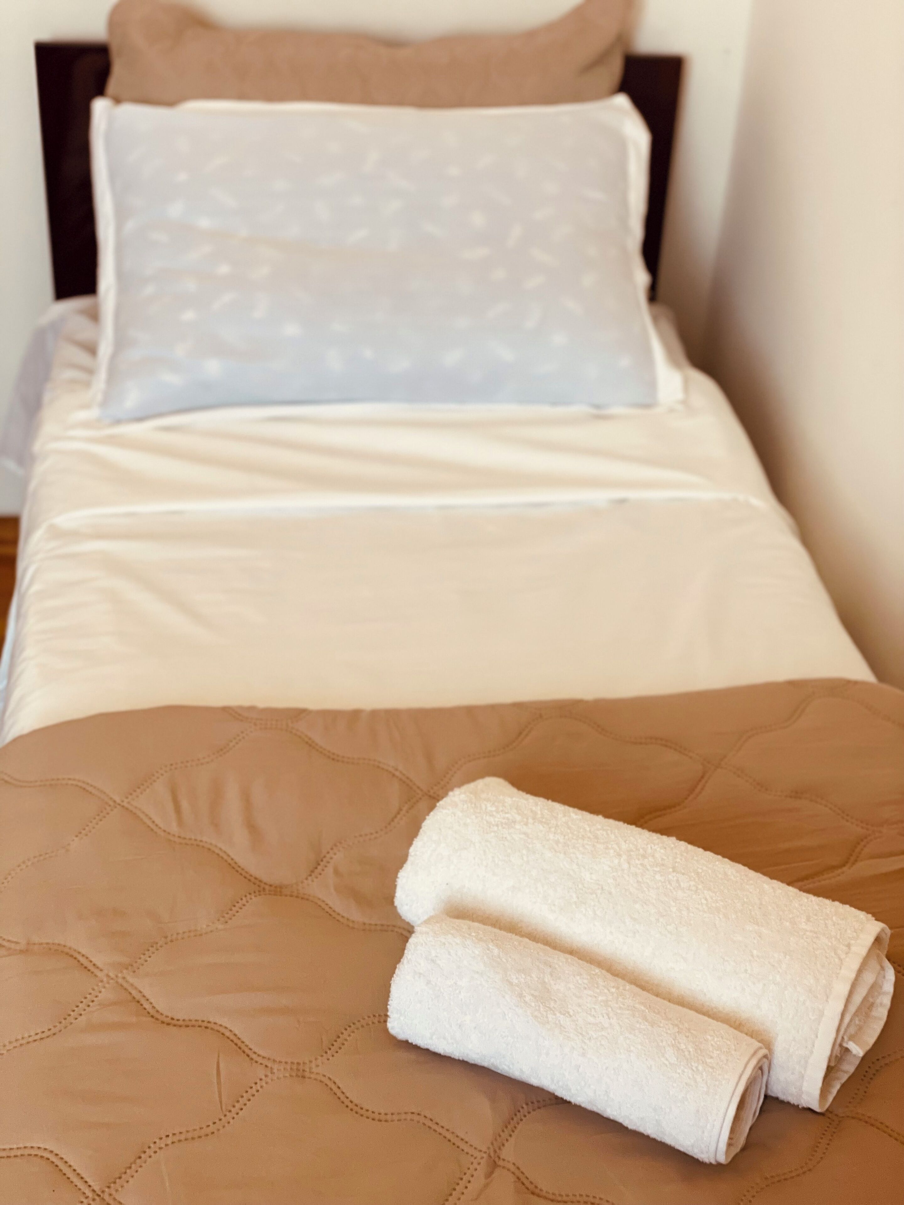 A neatly made bed with a brown quilt and two rolled white towels.