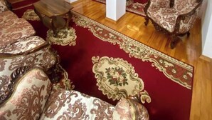 A spacious living room with a red carpet, wooden flooring, and ornate furniture. - House of Warmth (Baghdati)