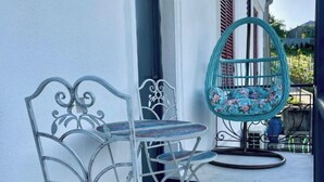 A balcony with a metal chair and a hanging chair, both with floral cushions. - House of Warmth (Baghdati)