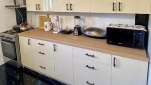 A modern kitchen with white cabinets, a black countertop, and a black marble floor. - House of Warmth (Baghdati)