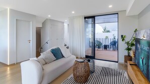 Una sala moderna con sofá, una mesa de centro y un ventanal corredero que da a un patio exterior con sillas y una mesa.