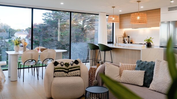 Una sala de estar moderna con un sofá, un comedor con sillas y una cocina con mostrador y electrodomésticos.
