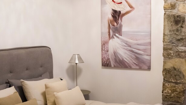 A bedroom with a bed, pillows, a lamp, a painting, and a stone wall. - Collio Suite (Cormons)
