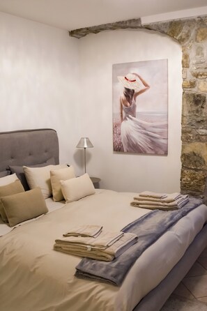 Een slaapkamer met een bed, kussens, een lamp, een schilderij en een stenen muur.