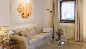 A living room with a beige sofa, a glass coffee table, a lamp, and a wall-mounted artwork. - Collio Suite (Cormons)