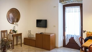 A living room with a television, a wooden cabinet, a dining table, and a door with a lace curtain. - Collio Suite (Cormons)