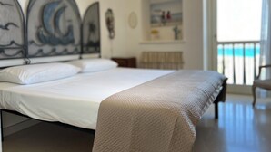 Ein Schlafzimmer mit einem Bett, einem Kopfteil mit Dekor, einem Nachttisch und einem Fenster mit Blick auf den Strand.