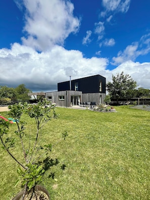 A modern two-story house with a flat roof, a chimney, and a covered patio area. - Maison en Bois , Ty Kérou (Mahalon)