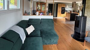 Una sala de estar moderna con un sofá seccional verde, piso de madera, una cocina al fondo y una chimenea.