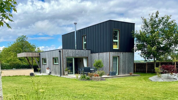 Una casa moderna de dos pisos con techo plano, ventanas amplias y una chimenea visible.