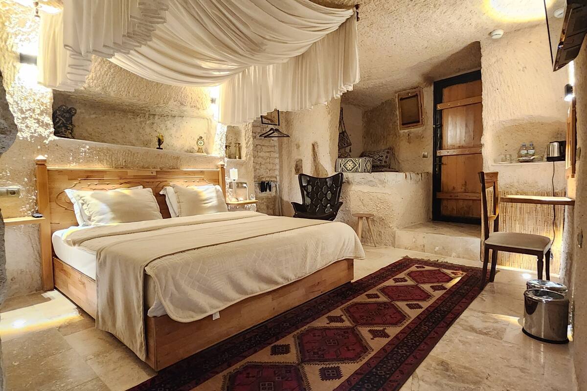 A rustic bedroom with a wooden bed, a patterned rug, and a stone wall.