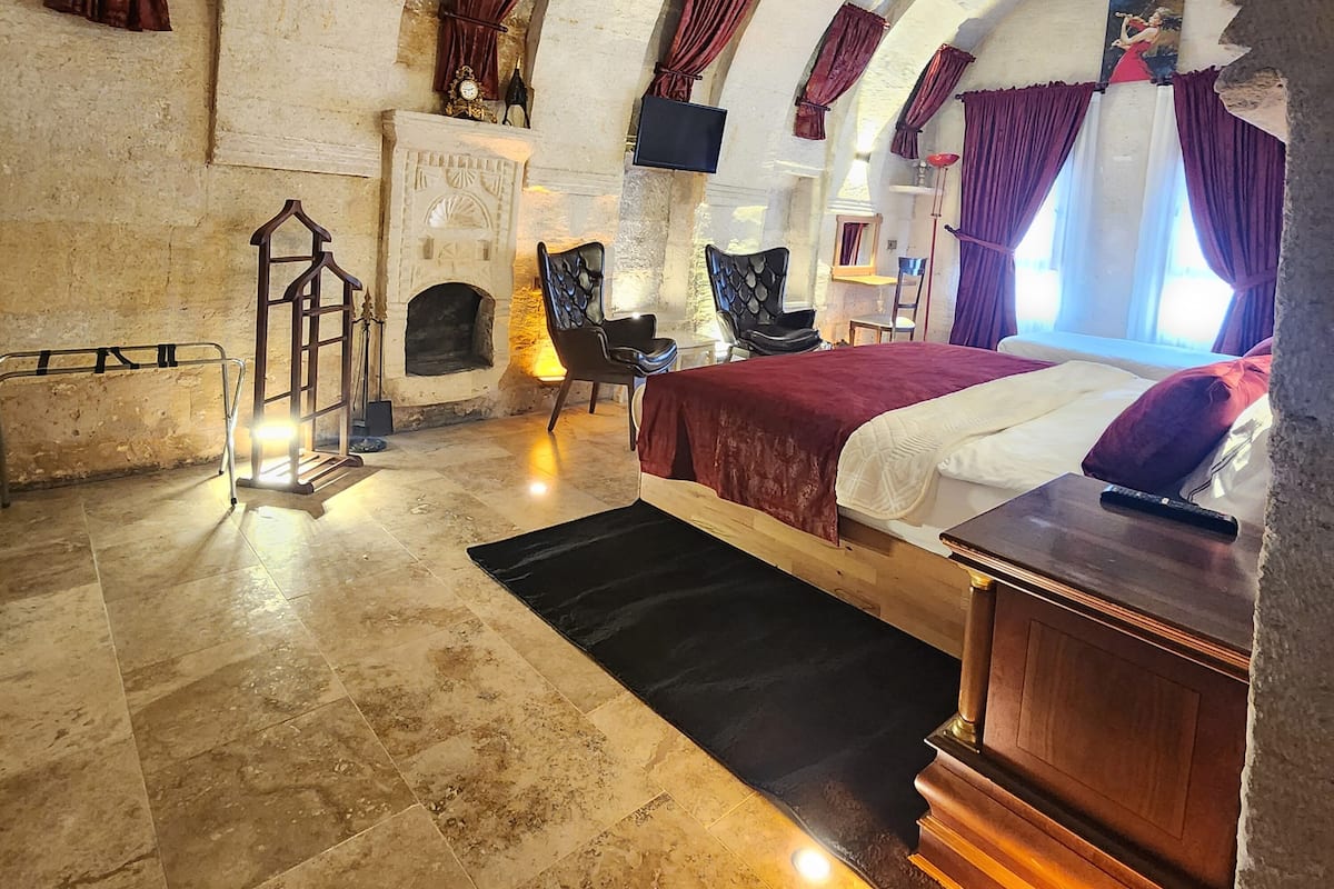 A room with a fireplace, a bed, a chair, and a TV.