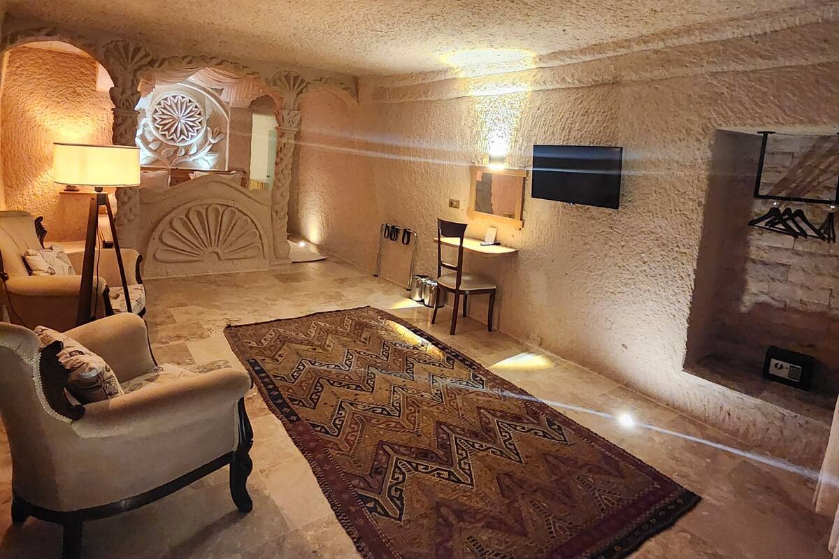 A cozy room with a stone wall, a patterned rug, a chair, a desk, and a TV mounted on the wall.