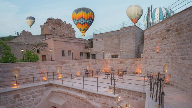Eine Dachterrasse mit Steinmauern, Sitzgelegenheiten im Freien und Heißluftballons im Hintergrund.