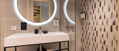 A modern bathroom with a white sink, two illuminated mirrors, a glass shower enclosure, and a patterned wall.