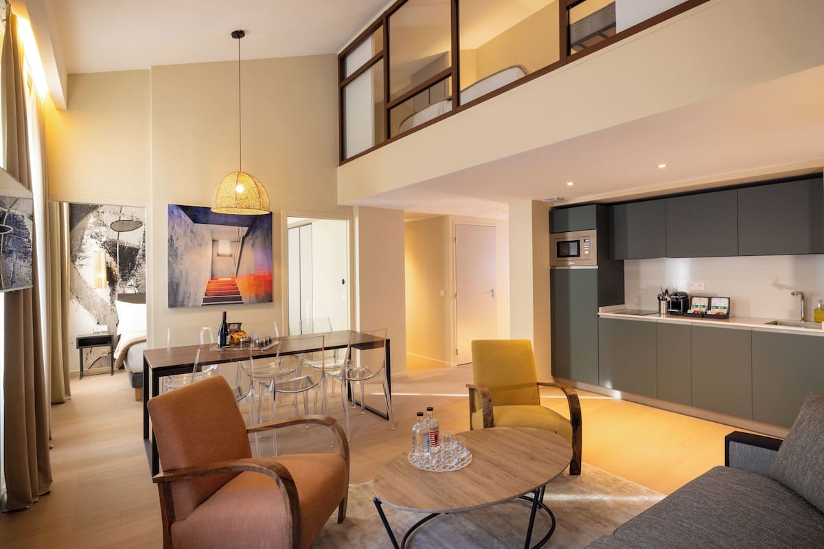 A modern living room with a dining area, a kitchen, and a staircase leading to an upper level.
