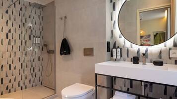 A modern bathroom with a glass-enclosed shower, a white toilet, and a large mirror above a white sink.