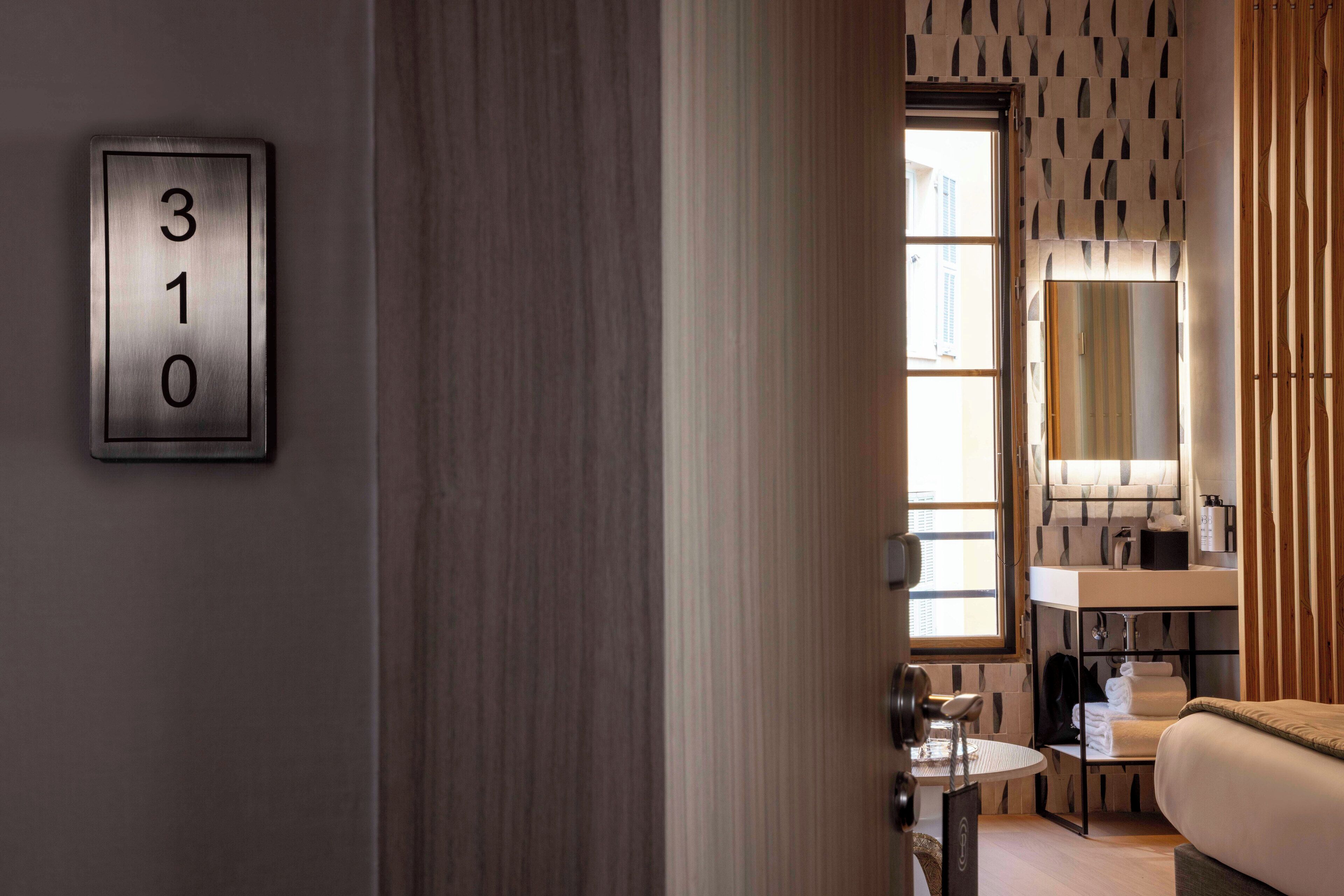 Una habitación de hotel moderna con un cartel con número, una ventana, un lavabo y un espejo.