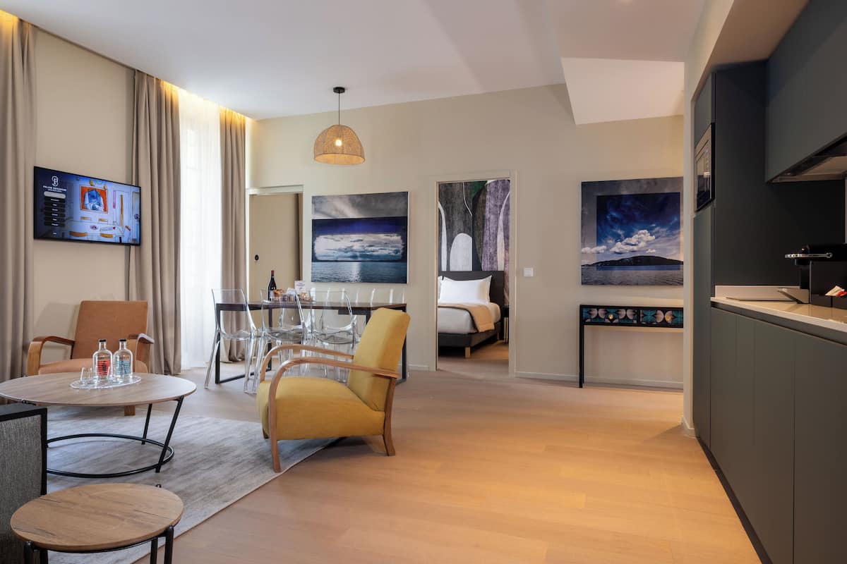 A modern hotel room with a dining area, a sofa, a TV, and artwork on the walls.