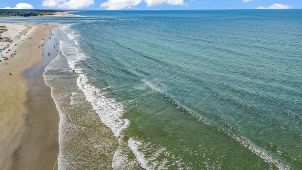 Una spiaggia con acqua cristallina, una battigia sabbiosa e alcune persone.