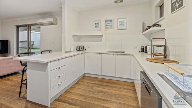Una cocina moderna con armarios blancos, una encimera de madera y un lavavajillas integrado. Hay tres cuadros en la pared, y una ventana proporciona luz natural.