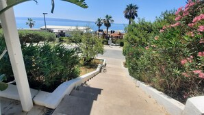 Un percorso che conduce a un edificio con vista sul mare, circondato da vegetazione e palme.
