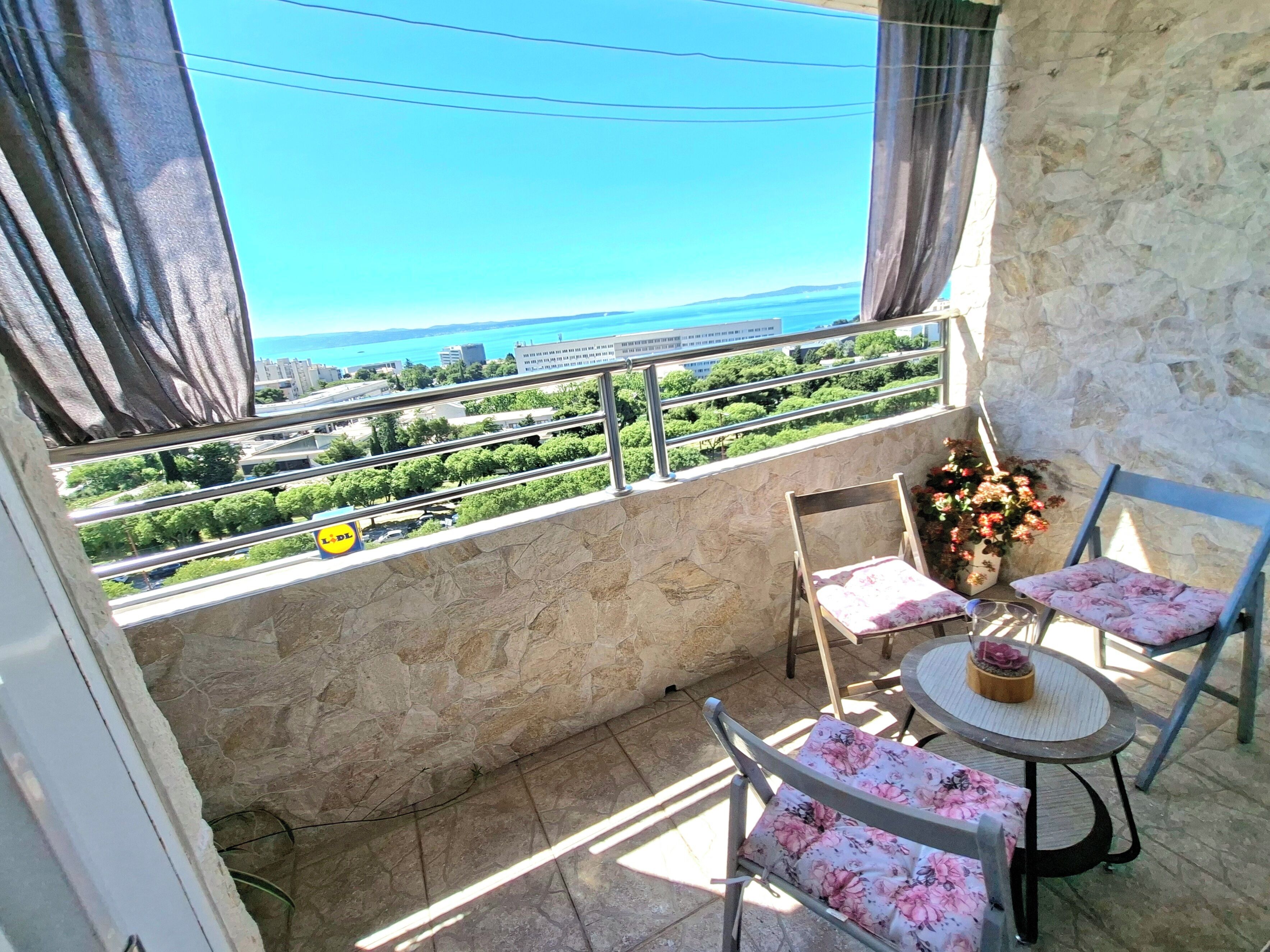 A balcony with a view of a cityscape, a table with chairs, and a flower vase.