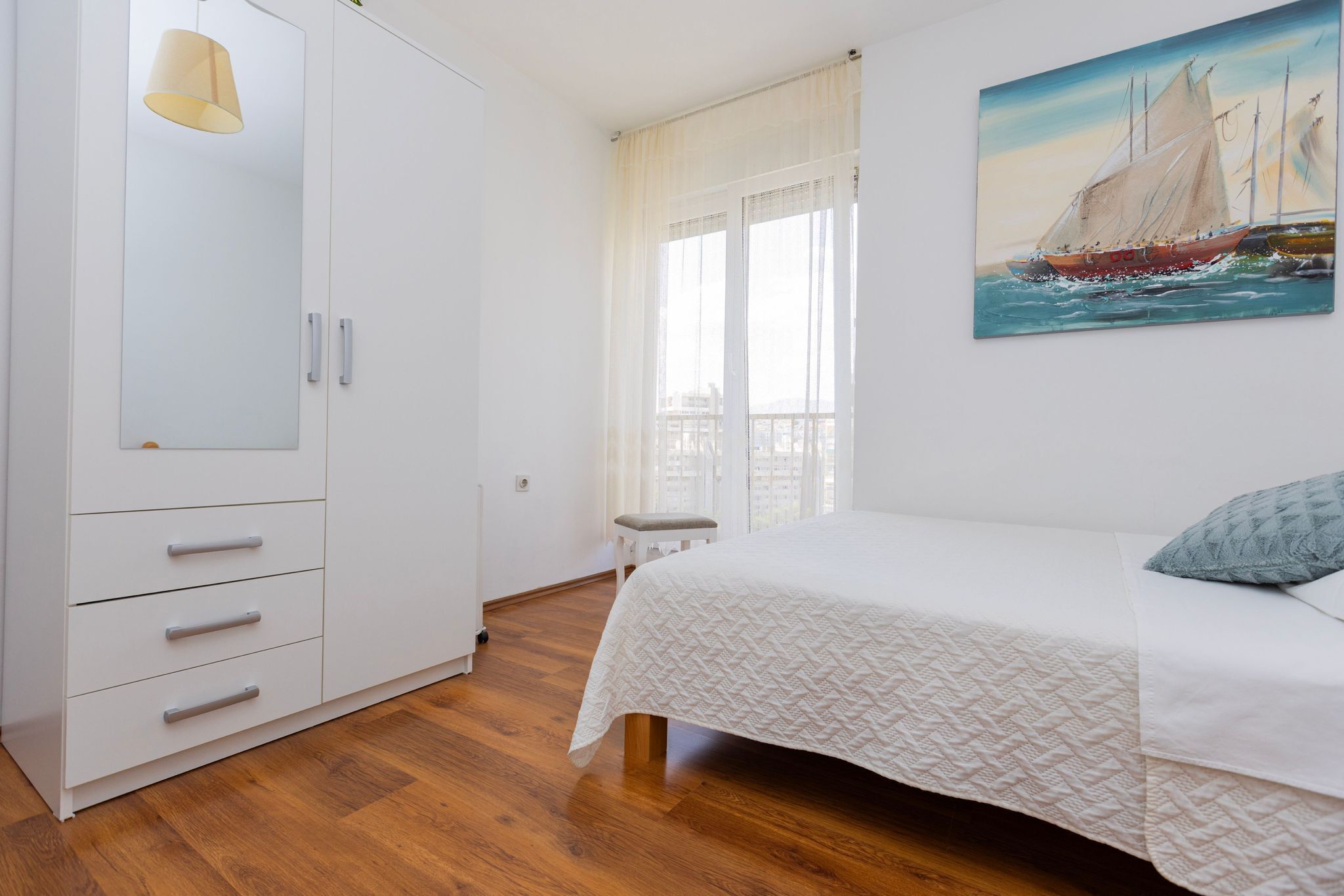 A bedroom with a bed, a wardrobe, a painting, and a window with curtains.