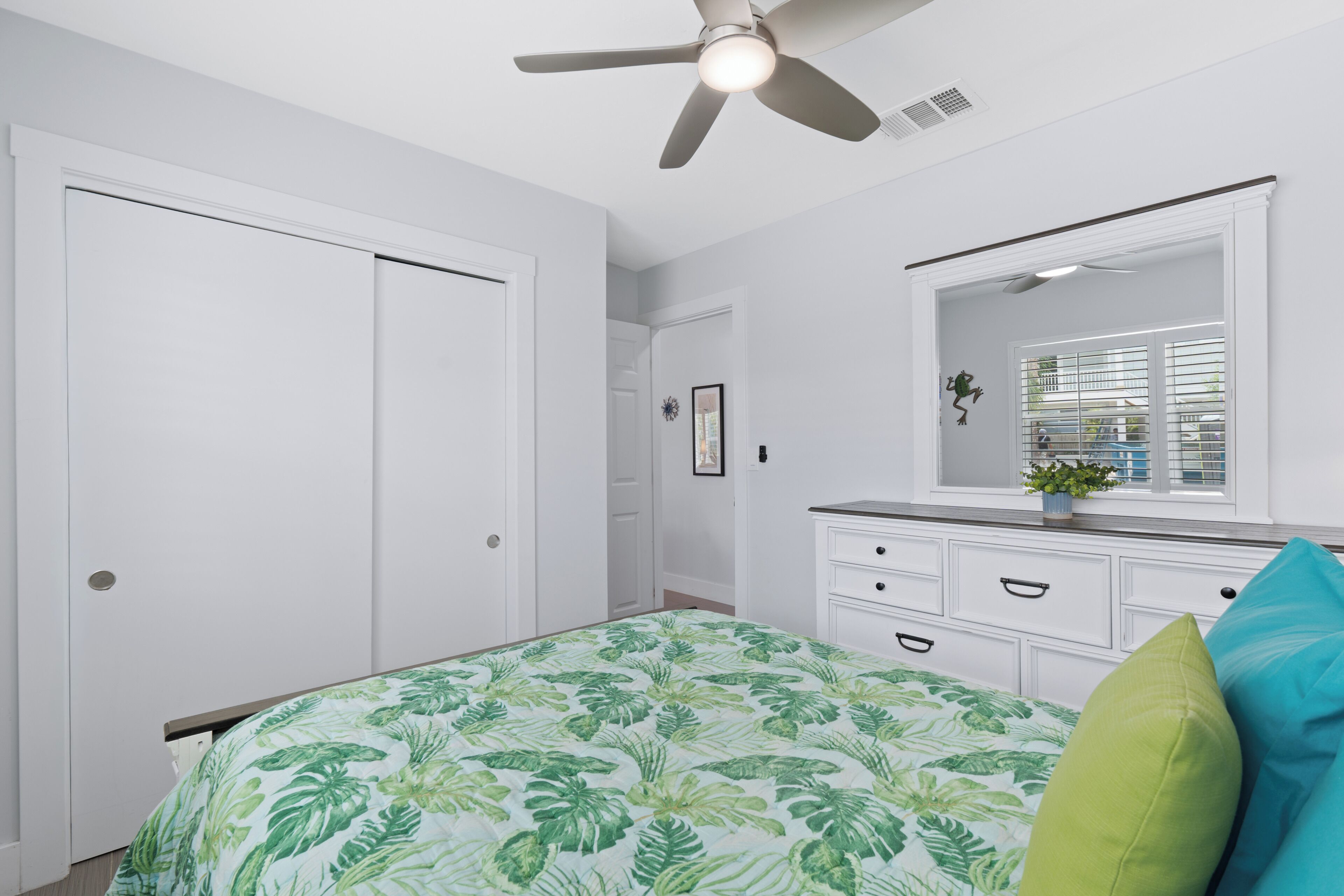 A bedroom with a bed, a dresser, a mirror, a ceiling fan, and a window with blinds.