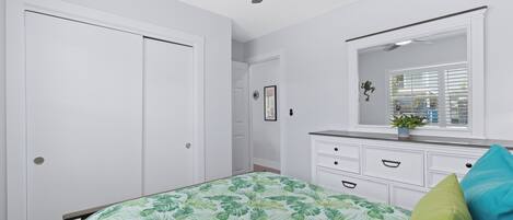 A bedroom with a bed, a dresser, a mirror, a ceiling fan, and a window with blinds.