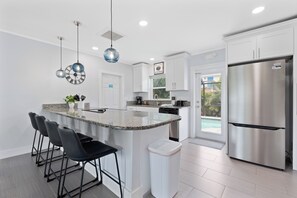 A modern kitchen with a central island, bar stools, a stainless steel refrigerator, and pendant lighting.