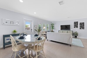 A modern living room with a dining area, white walls, and a flat-screen TV.