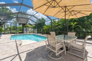 Un espacio exterior techado con piscina, una mesa de vidrio y sillas.