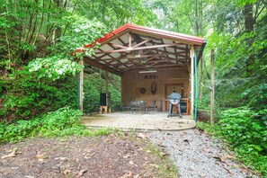Un espace extérieur aménagé, abrité et doté d’une structure en bois, d’un barbecue et d’un haut-parleur fixé au mur.
