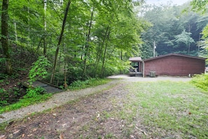 A rustic cabin with a gravel path leading to it, surrounded by dense forest.