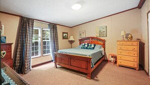 Un dormitorio con una cama de madera, un aparador, una ventana con cortinas y suelo cubierto de alfombra.