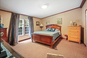 Un dormitorio con una cama de madera, un aparador, una ventana con cortinas y suelo cubierto de alfombra.