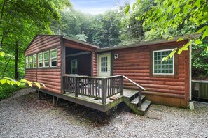 Une cabane en bois dotée d’un porche et d’une petite terrasse, entourée d’une forêt dense.