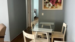 Un comedor con una mesa de vidrio y cuatro sillas, un cuadro de flores en la pared y un libro rojo sobre una mesa.