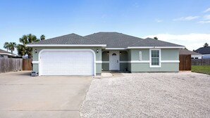 A single-story house with a garage, a front porch, and a gravel driveway. - Dog-Friendly Island Retreat | Private Home & Large Yard (Corpus Christi)