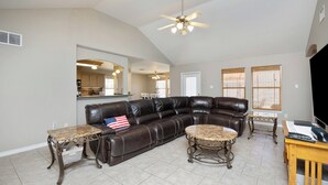 A spacious living room with a leather sectional sofa, a ceiling fan, and a kitchen visible through an archway. - Dog-Friendly Island Retreat | Private Home & Large Yard (Corpus Christi)