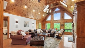 Amplia sala de estar con techos de madera y ventanas grandes, amueblada con sofás de cuero y una mesa de centro.