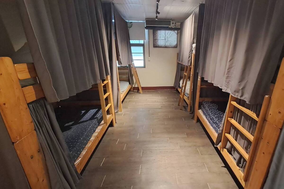 A narrow corridor with bunk beds on either side, wooden flooring, and a ceiling fan.