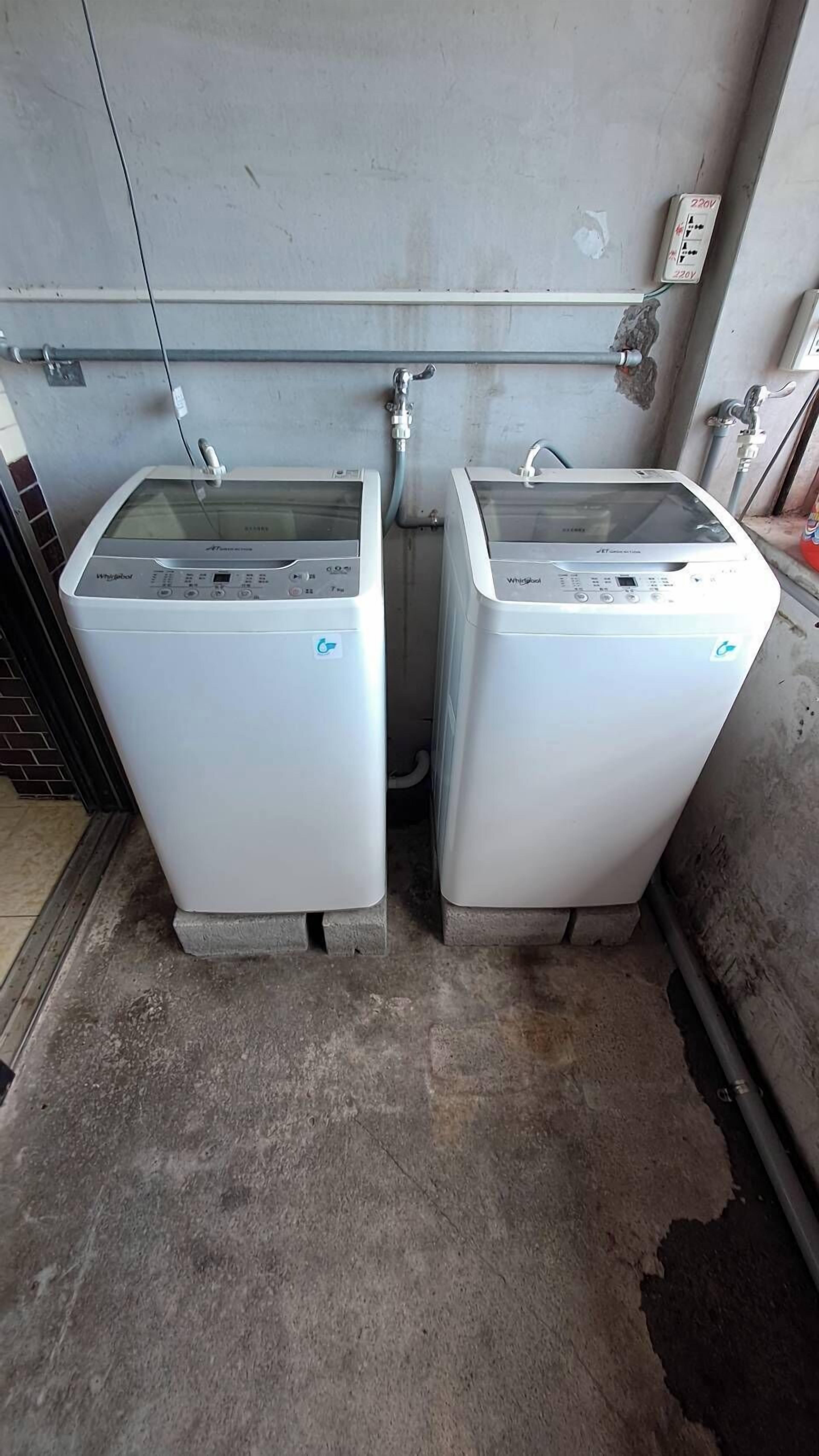 Two Whirlpool washing machines in a utility room with a concrete floor and a metal wall.