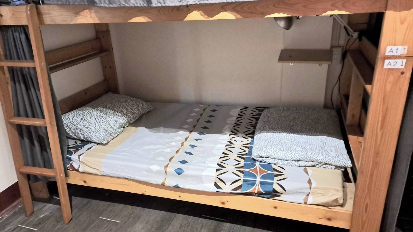 A bunk bed with a ladder on the left, a headboard on the right, and a wall-mounted shelf above.
