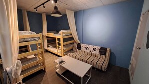 Une chambre de dortoir avec des lits superposés, un canapé à rayures, une petite table et un ventilateur de plafond.
