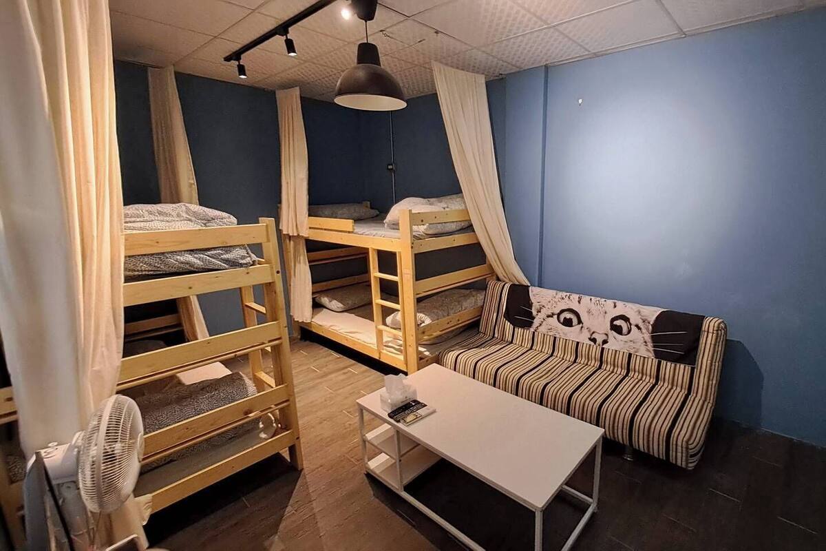 A dormitory room with bunk beds, a striped sofa, a small table, and a ceiling fan.
