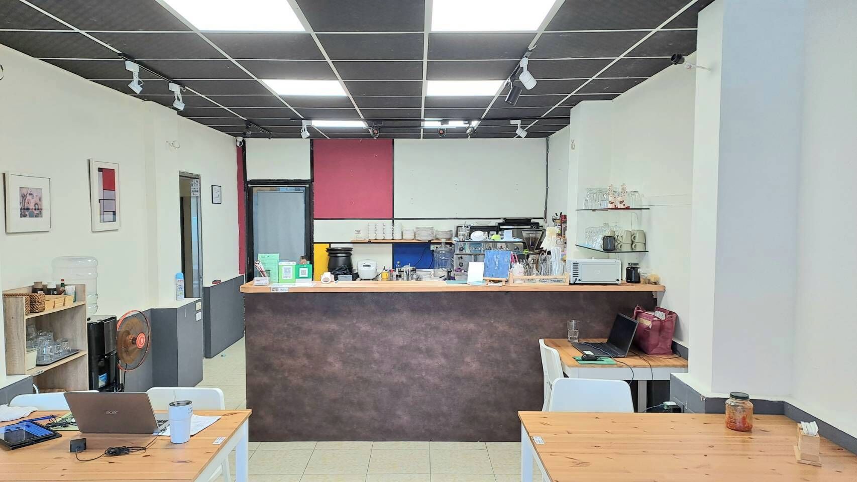 A small, modern office with a reception desk, a coffee machine, and various office supplies.