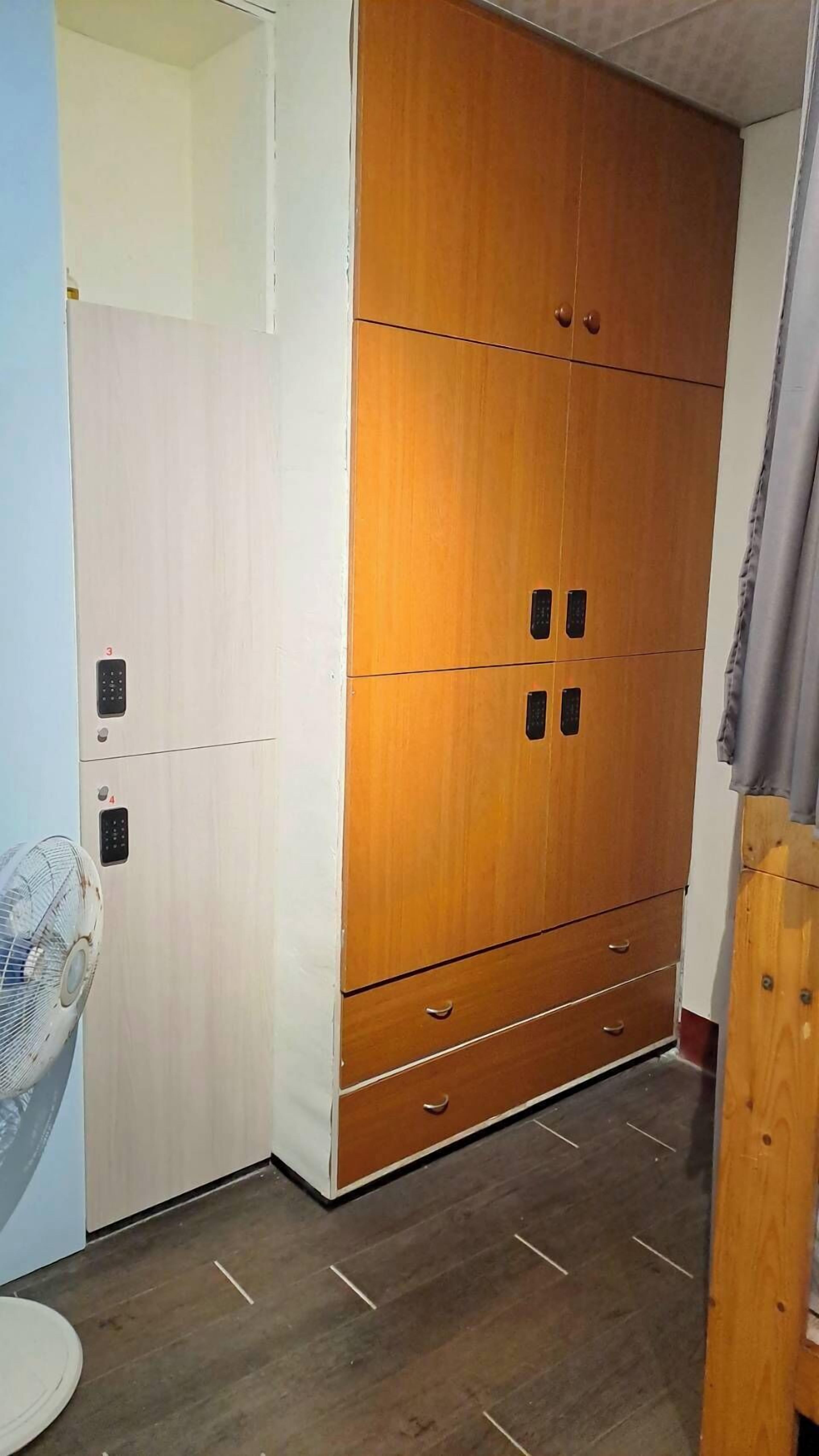 A room with a large wooden wardrobe, a white cabinet, and a fan.