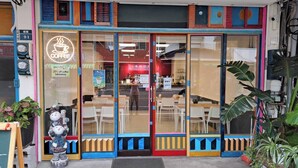 Une devanture colorée, avec une enseigne au néon représentant une tasse de café, des portes vitrées et des tables visibles à l’intérieur par les fenêtres.